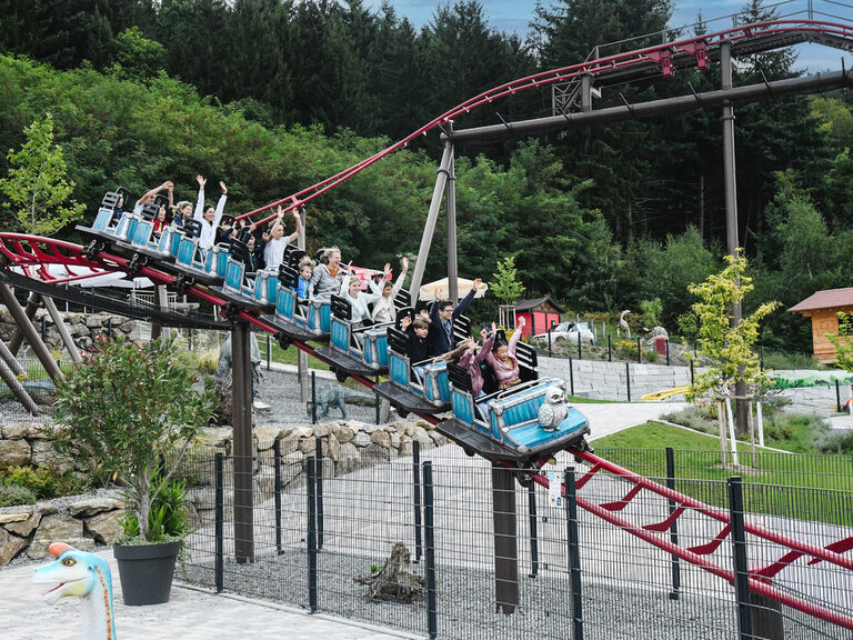 Gäste haben lachend Spaß in der Dinoachterbahn des Freizeitparks "Edelwies" in Neukirchen.